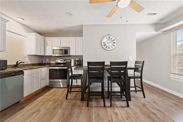 820 Peach Tree Ln, Blue Springs, MO 64064 - kitchen featuring stainless steel appliances, white cabinetry, light wood-style floors, a textured ceiling, and ceiling fan