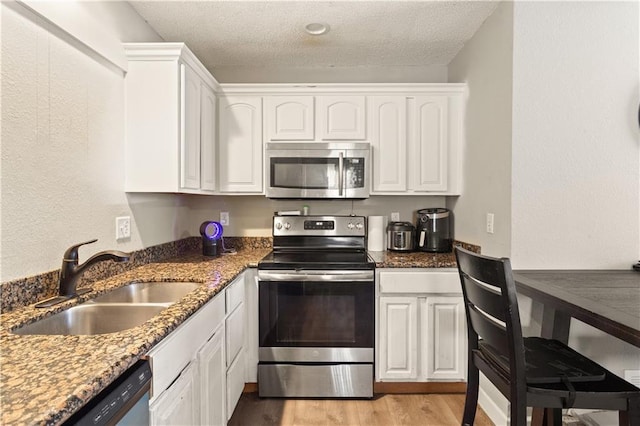 820 Peach Tree Ln, Blue Springs, MO 64064 - kitchen featuring stainless steel appliances, light wood-style floors, white cabinetry, dark stone counters, and a textured ceiling