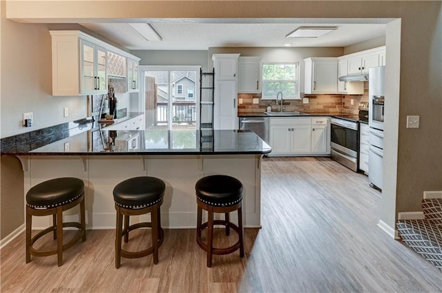 3524 NE Austin Dr, Lees Summit, MO 64064 - kitchen with light wood-type flooring, appliances with stainless steel finishes, a peninsula, white cabinets, and backsplash
