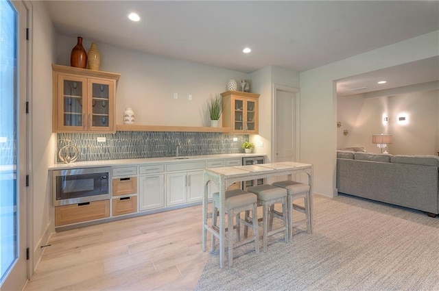 7736 N Donnelly Ave, Kansas City, MO 64158 - kitchen featuring stainless steel microwave, light countertops, glass insert cabinets, recessed lighting, and backsplash