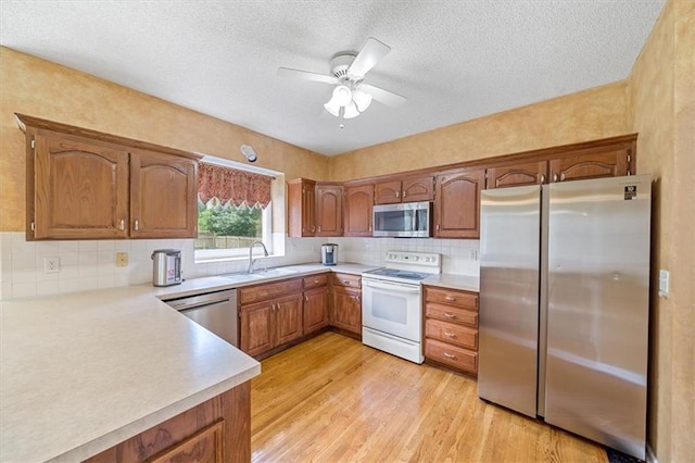 6715 W 148th Ter, Overland Park, KS 66223 - kitchen with stainless steel appliances, brown cabinetry, light countertops, ceiling fan, and light wood-style flooring