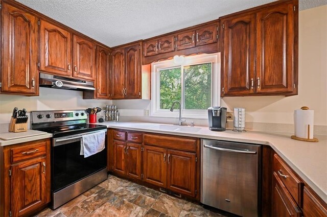 1621 Vilas St, Leavenworth, KS 66048 - kitchen featuring stainless steel appliances, under cabinet range hood, light countertops, a textured ceiling, and brown cabinetry