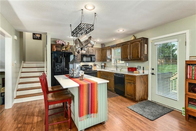 407 Maple Ct, Lansing, KS 66043 - kitchen with black appliances, light countertops, a kitchen island, light wood-style flooring, and dark brown cabinets