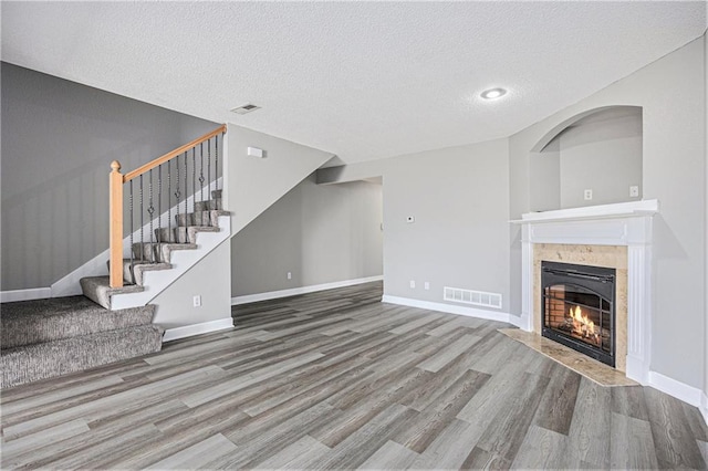 902 SW Peach Tree Ln, Blue Springs, MO 64064 - unfurnished living room with wood finished floors, stairway, a tiled fireplace, and a textured ceiling