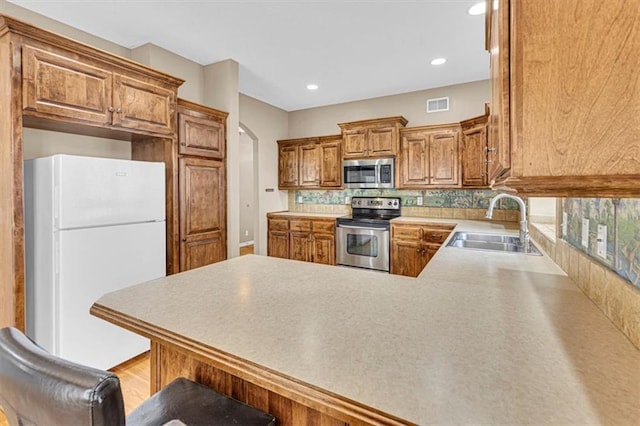 895 N Diane Dr, Olathe, KS 66061 - kitchen with stainless steel appliances, a peninsula, brown cabinetry, decorative backsplash, and recessed lighting
