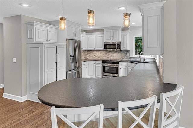 14440 W 187th Ter, Olathe, KS 66062 - kitchen featuring stainless steel appliances, dark countertops, a peninsula, wood finished floors, and decorative backsplash