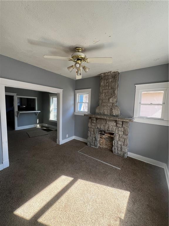 4902 E 17th St, Kansas City, MO 64127 - unfurnished living room with a textured ceiling, ceiling fan, carpet, and a fireplace
