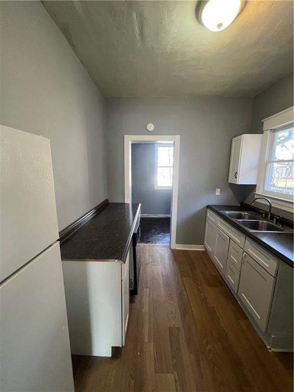 4902 E 17th St, Kansas City, MO 64127 - kitchen with freestanding refrigerator, dark countertops, dark wood-type flooring, and plenty of natural light