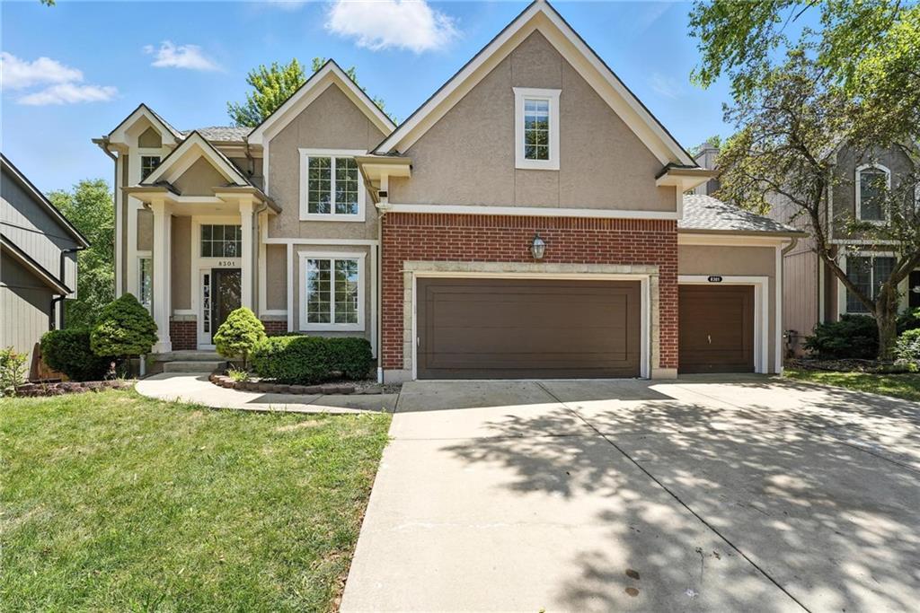 8301 W 156th St, Overland Park, KS 66223 - traditional home with concrete driveway, stucco siding, a front yard, and brick siding