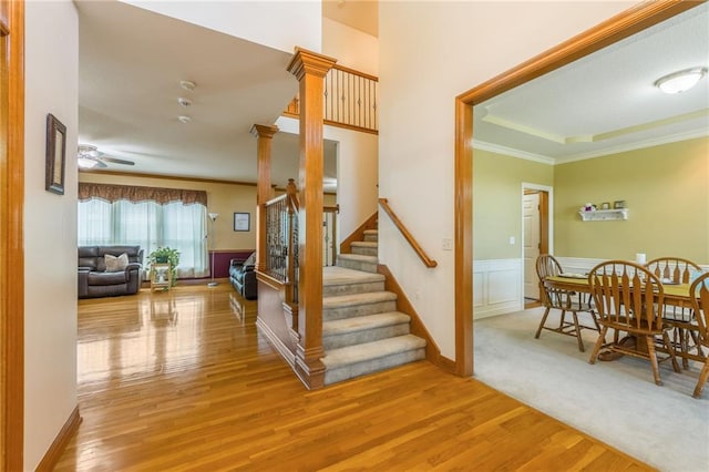4000 SW Boulder Dr, Lees Summit, MO 64082 - stairway featuring crown molding, wood finished floors, ceiling fan, wainscoting, and decorative columns