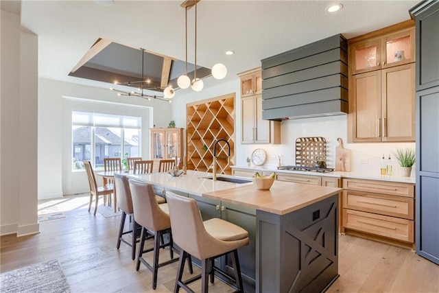 17325 Bradshaw St, Overland Park, KS 66221 - kitchen featuring range hood, stainless steel gas cooktop, a kitchen island with sink, light wood-style flooring, and a kitchen breakfast bar