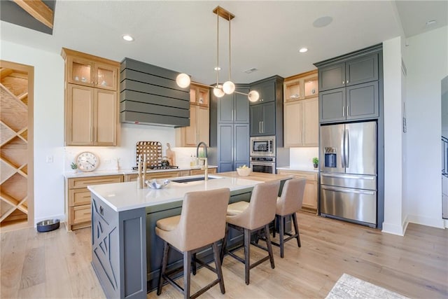 17325 Bradshaw St, Overland Park, KS 66221 - kitchen with appliances with stainless steel finishes, range hood, light countertops, a kitchen island with sink, and light wood-style floors