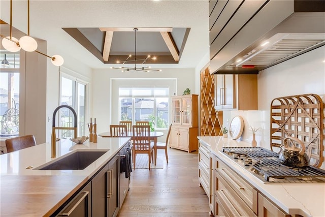 17325 Bradshaw St, Overland Park, KS 66221 - kitchen featuring wall chimney range hood, stainless steel gas stovetop, a chandelier, light wood finished floors, and a tray ceiling