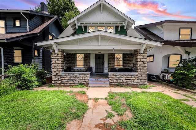 3443 Agnes Ave, Kansas City, MO 64128 - view of front of house with stone siding, a porch, a chimney, a front yard, and roof with shingles