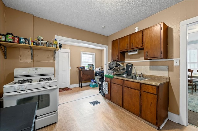 3443 Agnes Ave, Kansas City, MO 64128 - kitchen featuring white gas stove, brown cabinetry, and a textured ceiling
