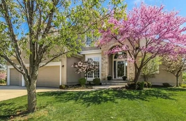 14301 Beverly St, Overland Park, KS 66223 - view of property hidden behind natural elements featuring driveway, a front yard, stucco siding, and an attached garage