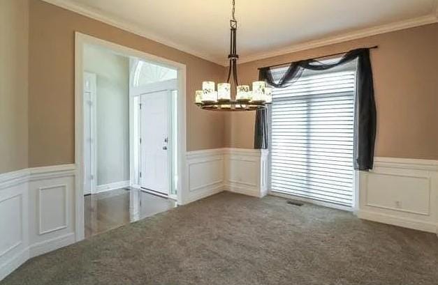 14301 Beverly St, Overland Park, KS 66223 - unfurnished dining area featuring a chandelier, ornamental molding, a wainscoted wall, carpet flooring, and a decorative wall