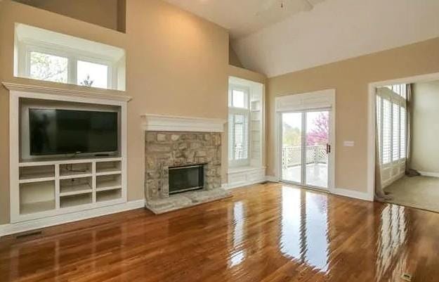 14301 Beverly St, Overland Park, KS 66223 - unfurnished living room featuring wood finished floors, a stone fireplace, and high vaulted ceiling