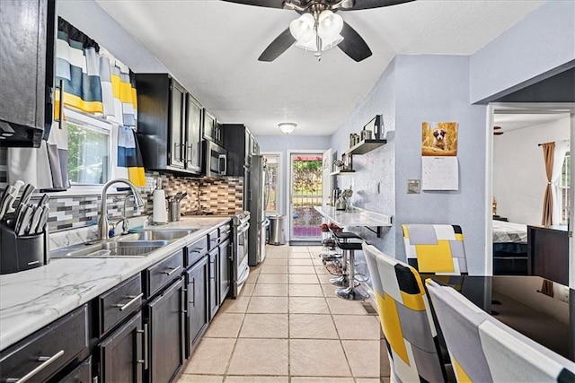 3021 Topping Ave, Kansas City, MO 64129 - kitchen with appliances with stainless steel finishes, backsplash, a ceiling fan, light tile patterned floors, and dark cabinetry