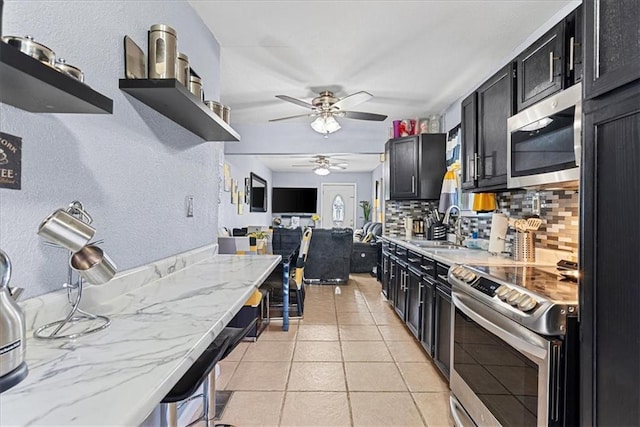3021 Topping Ave, Kansas City, MO 64129 - kitchen featuring stainless steel appliances, dark cabinets, ceiling fan, tasteful backsplash, and a textured wall