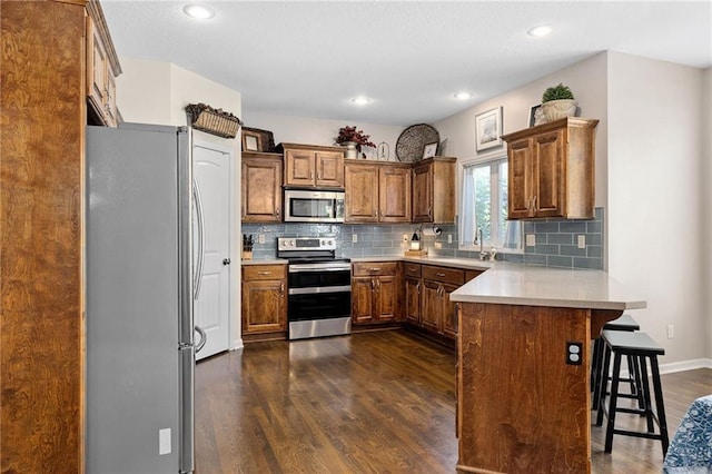14920 S Roxburghe St, Olathe, KS 66061 - kitchen with stainless steel appliances, a peninsula, dark wood-style flooring, backsplash, and recessed lighting