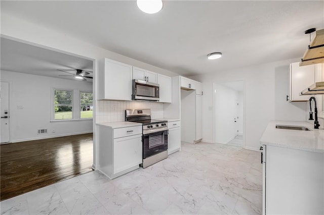 7909 Arnote Rd, Pleasant Valley, MO 64068 - kitchen with appliances with stainless steel finishes, light marble finish flooring, ceiling fan, white cabinets, and backsplash