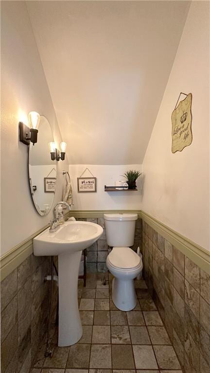 309 College St, Paola, KS 66071 - half bathroom featuring lofted ceiling, tile walls, and a wainscoted wall
