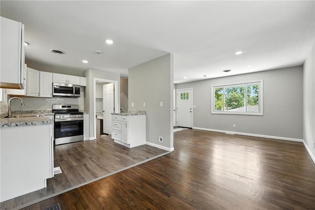 4916 N Manchester Ave, Kansas City, MO 64119 - kitchen featuring stainless steel appliances, white cabinets, open floor plan, dark wood finished floors, and light stone countertops
