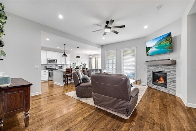 1296 NW Lindenwood Dr, Grain Valley, MO 64029 - living room with dark wood-type flooring, a ceiling fan, a stone fireplace, and recessed lighting