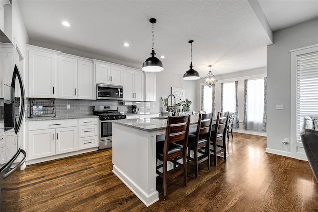 1296 NW Lindenwood Dr, Grain Valley, MO 64029 - kitchen with stainless steel appliances, recessed lighting, tasteful backsplash, an island with sink, and dark wood finished floors
