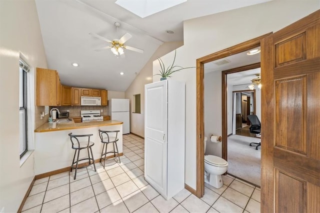 362 S 10th St, Kansas City, KS 66102 - kitchen featuring white appliances, a skylight, vaulted ceiling, a peninsula, and decorative backsplash