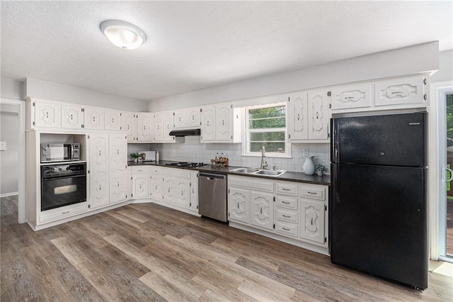 12731 Byars Rd, Grandview, MO 64030 - kitchen featuring black appliances, dark countertops, under cabinet range hood, dark wood-type flooring, and a textured ceiling