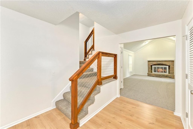 805 NW 18th St, Blue Springs, MO 64015 - stairs with wood finished floors, lofted ceiling, a brick fireplace, and a textured ceiling