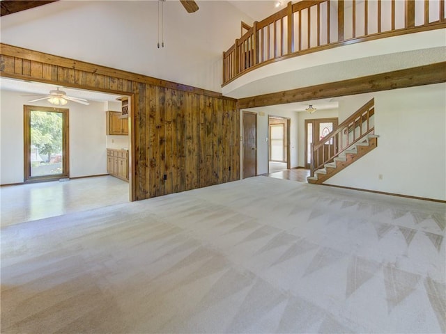 4008 NE 57th Ter, Kansas City, MO 64119 - unfurnished living room featuring ceiling fan, light colored carpet, high vaulted ceiling, stairs, and wood walls