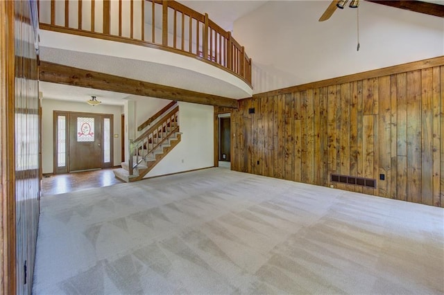 4008 NE 57th Ter, Kansas City, MO 64119 - unfurnished living room with carpet floors, wooden walls, stairs, a ceiling fan, and a towering ceiling