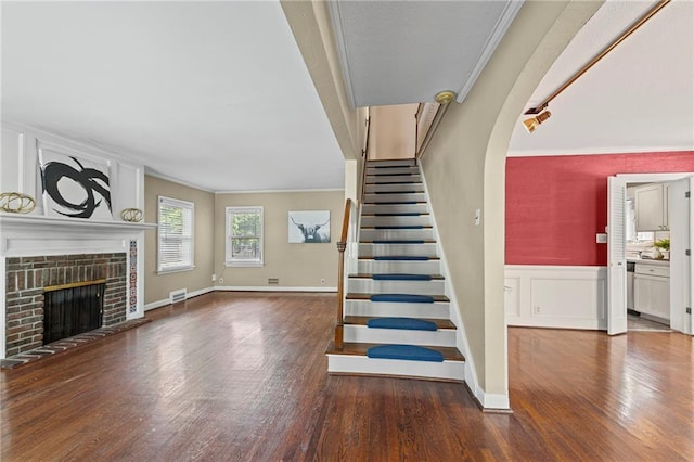 1296 W 72nd Ter, Kansas City, MO 64114 - staircase featuring wood finished floors, ornamental molding, a fireplace, wainscoting, and a decorative wall