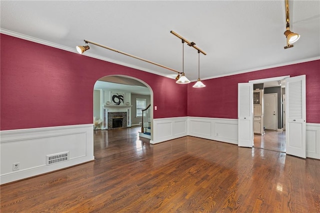 1296 W 72nd Ter, Kansas City, MO 64114 - spare room with a wainscoted wall, rail lighting, crown molding, wood finished floors, and a brick fireplace