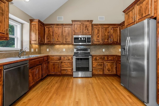 701 Tomahawk Ct, Smithville, MO 64089 - kitchen featuring appliances with stainless steel finishes, lofted ceiling, light wood-style flooring, backsplash, and brown cabinets