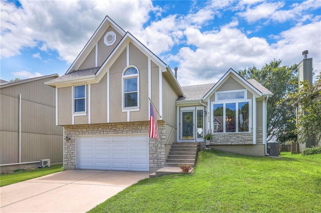 21509 W 52nd St, Shawnee, KS 66226 - view of front of home with stone siding, driveway, a front yard, a garage, and stucco siding