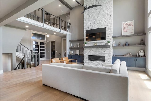 1113 Hummingbird Ct, Greenwood, MO 64034 - living room featuring a stone fireplace, wood finished floors, a towering ceiling, a ceiling fan, and stairs