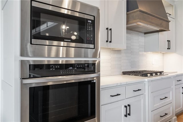 1113 Hummingbird Ct, Greenwood, MO 64034 - kitchen featuring appliances with stainless steel finishes, custom range hood, white cabinetry, and backsplash
