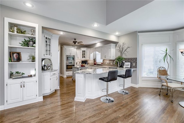 1021 SW Summit Falls Dr, Lees Summit, MO 64081 - kitchen with stainless steel appliances, ceiling fan, a peninsula, glass insert cabinets, and wood finished floors