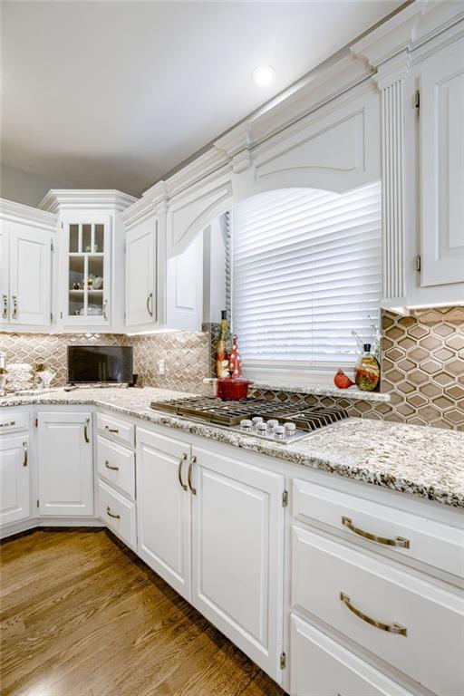 1021 SW Summit Falls Dr, Lees Summit, MO 64081 - kitchen with white cabinets, tasteful backsplash, stainless steel gas stovetop, glass insert cabinets, and light wood finished floors