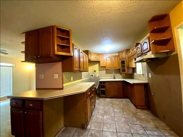 4738 Norton Cir, Kansas City, MO 64128 - kitchen with open shelves, a textured ceiling, light tile patterned floors, brown cabinets, and a peninsula