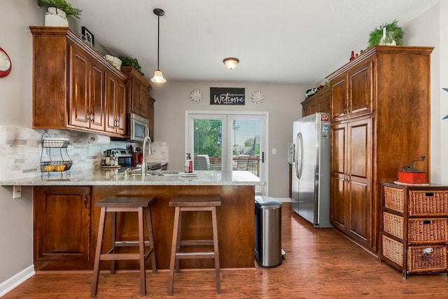 1912 Sequoia Dr, Raymore, MO 64083 - kitchen featuring appliances with stainless steel finishes, a peninsula, tasteful backsplash, dark wood-style floors, and decorative light fixtures