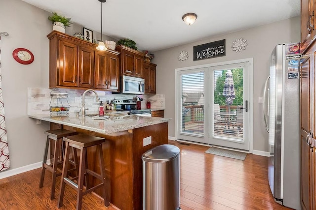 1912 Sequoia Dr, Raymore, MO 64083 - kitchen featuring stainless steel appliances, a peninsula, tasteful backsplash, wood finished floors, and a breakfast bar area