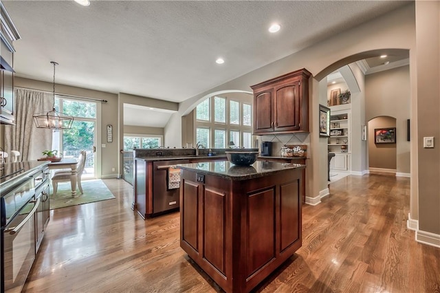 9638 Zarda Dr, Lenexa, KS 66227 - kitchen with stainless steel appliances, a kitchen island, dark stone countertops, arched walkways, and wood finished floors