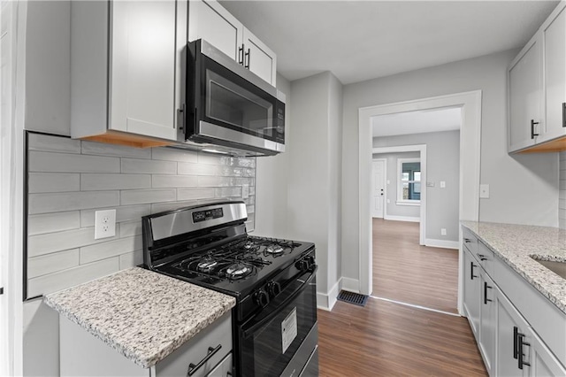 320 N Cedar Ave, Independence, MO 64053 - kitchen featuring black range with gas cooktop, stainless steel microwave, backsplash, dark wood-style flooring, and light stone countertops