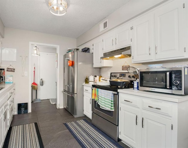 7921 Yecker St, Kansas City, KS 66102 - kitchen with under cabinet range hood, stainless steel appliances, white cabinets, light countertops, and dark tile patterned floors