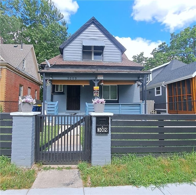 3009 Montgall Ave, Kansas City, MO 64128 - view of front facade with a porch, a fenced front yard, a gate, and a shingled roof